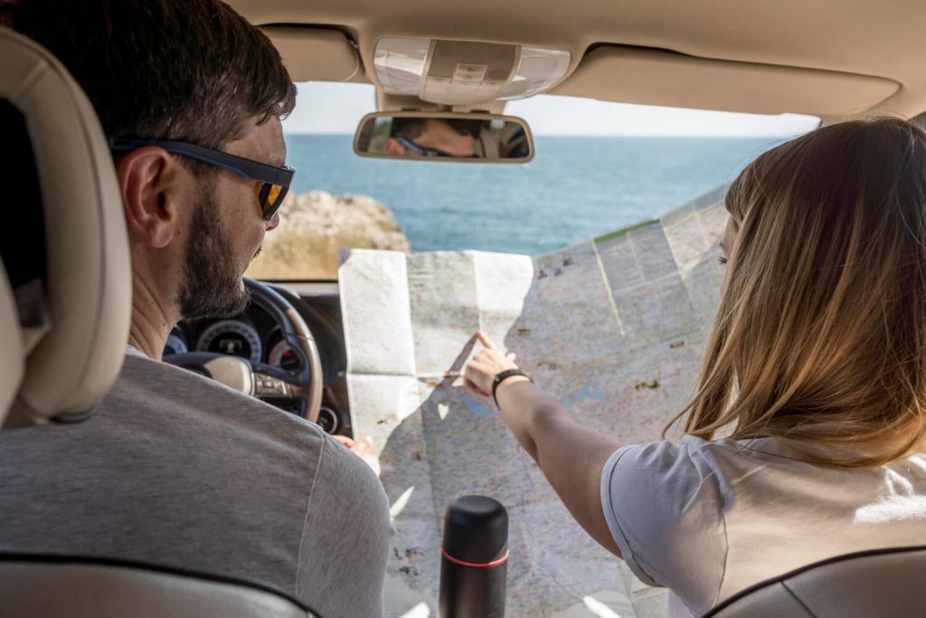 A couple is driving in Greece. They are inside a car, exploring a map.