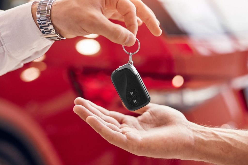 Thematic image for rental car safety tips. A salesman gives car keys to a renter.